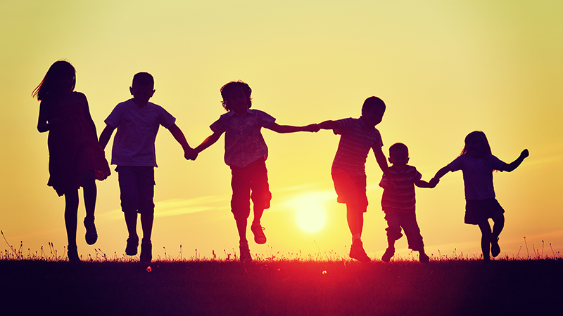 Silhouettes of six kids hand in hand towards a sunset 