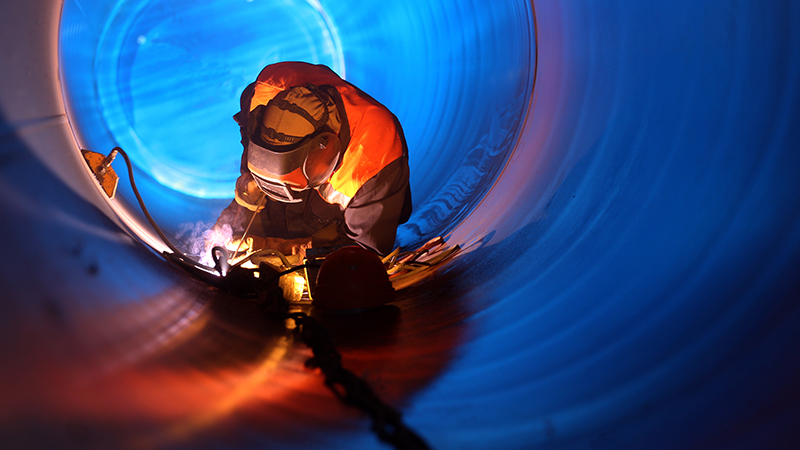 Industry worker welding inside an oil and gas pipe